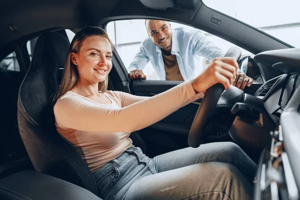 Fröhliches junges Paar schaut sich in einem neuen Auto um, das sie in einem Autohaus kaufen werden — Stockfoto