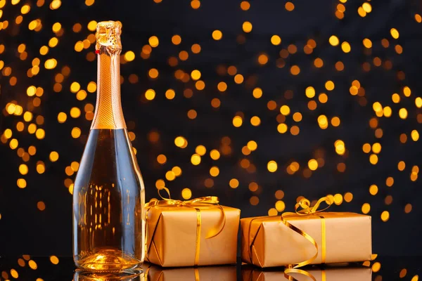 Şampanya şişesi ve Noel ışıklarının bulanık arka planına sarılmış hediye.