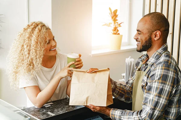 Sorridente donna bionda che parla con un cameriere di una caffetteria al bancone — Foto Stock