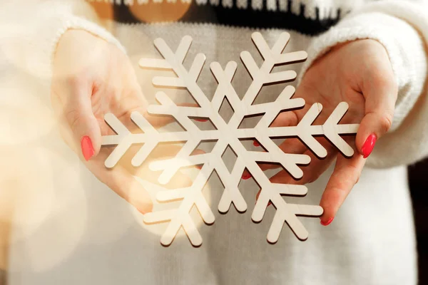 Manos femeninas sosteniendo juguete de Navidad de madera con luces borrosas — Foto de Stock