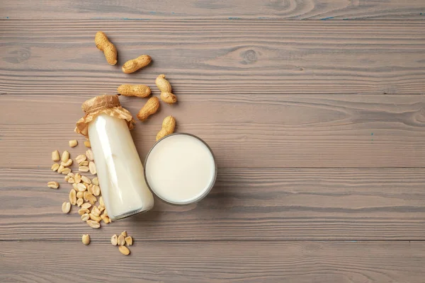 Арахисовое молоко в стеклянной бутылке с арахисом на деревянной доске — стоковое фото