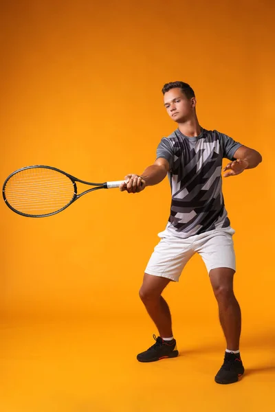Ολο το μήκος πορτρέτο ενός παίκτη του τένις σε δράση σε πορτοκαλί φόντο — Φωτογραφία Αρχείου