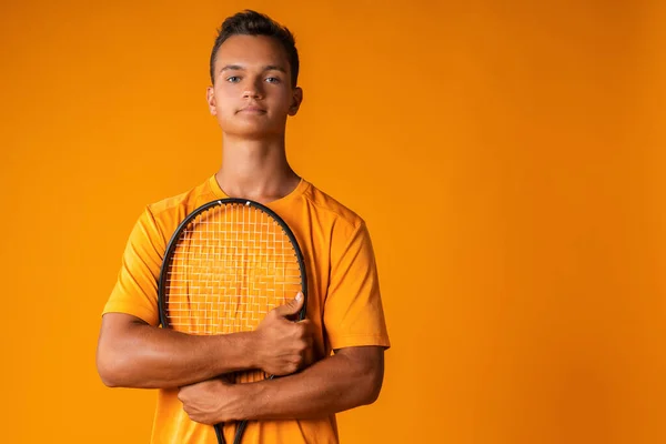 Estúdio tiro de um jovem jogador de tênis segurando raquete contra fundo laranja — Fotografia de Stock