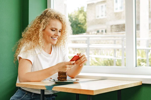 Mulher loira atraente sentada no café e usando seu telefone celular — Fotografia de Stock