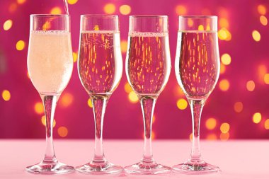 Pembe arka planda dört şampanya bardağı ve bulanık çelenk.