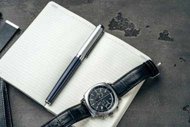 Koyu gri masaya erkek saati ve not defteri.