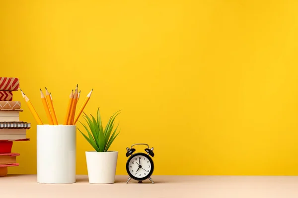 Tasse mit Bleistiften und Notizblöcken auf dem Schreibtisch vor gelbem Hintergrund — Stockfoto