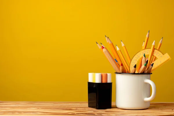 Служебный стаканчик с ручкой и канцелярскими принадлежностями на желтом фоне — стоковое фото