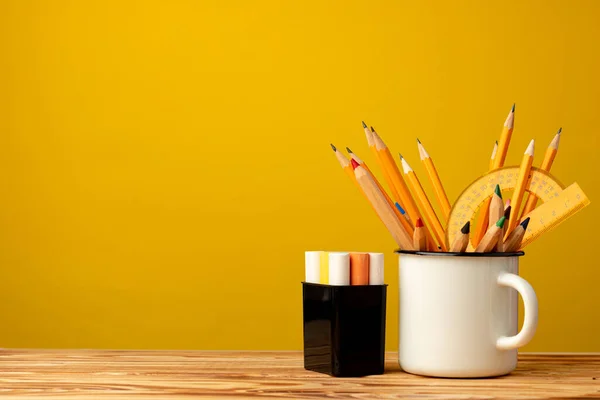 Copo de escritório com lápis e artigos de papelaria contra fundo amarelo — Fotografia de Stock