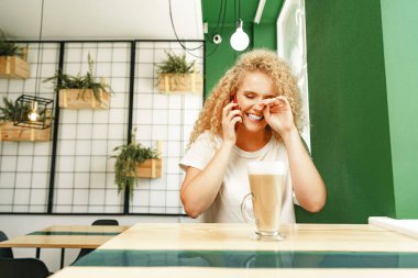 Kafeteryada genç ve güzel bir kadın telefonda konuşuyor.
