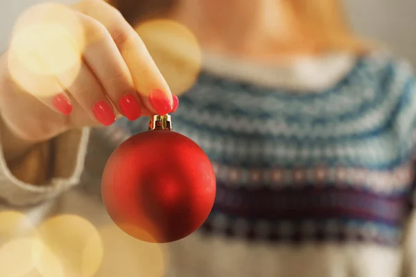 Mano de una mujer en jersey festivo con adornos navideños con luces borrosas — Foto de Stock