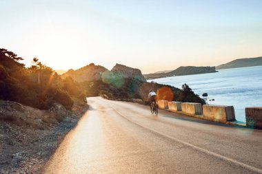 Bisikletli, sahil yolunda bisiklete biniyor.