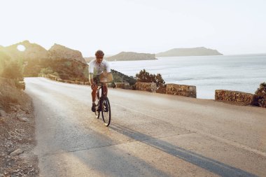 Bisikletli, sahil yolunda bisiklete biniyor.