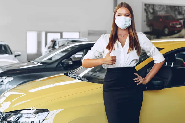 Woman car seller standing near new car wearing protective face mask