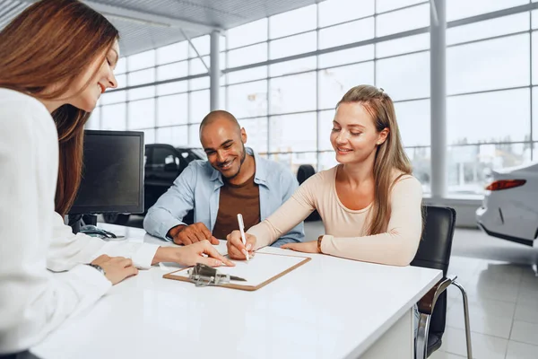 Vackra unga par skyltar dokument på bilhandlare showroom — Stockfoto