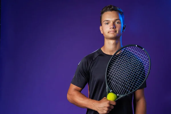 Caucasian young man tennis player posing with tennis racket against purple background