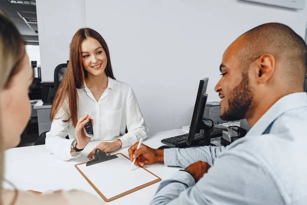 Ung kvinna bilhandlare visar kontrakt med ett par bilköpare — Stockfoto