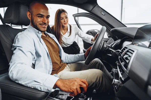 Jonge aantrekkelijke vrouw verkoper in auto showroom tonen een auto aan haar mannelijke klant — Stockfoto