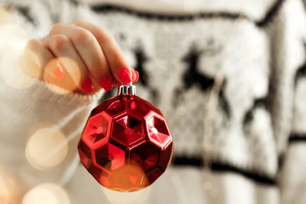 Mano di una donna in maglione festivo che tiene la bagattella natalizia con luci sfocate — Foto Stock