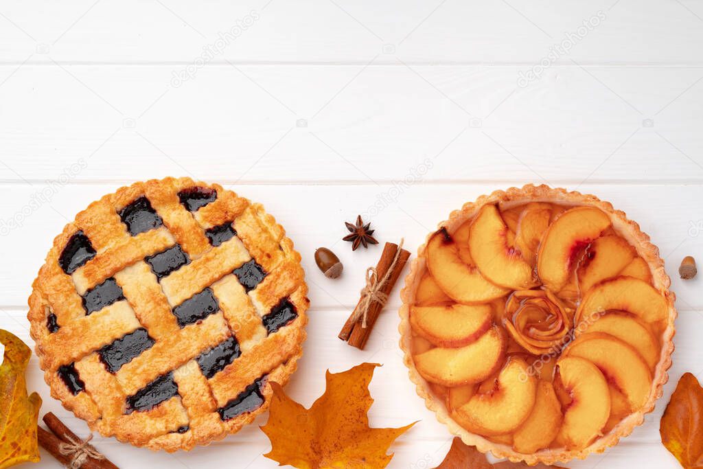 Autumn thankgiving pies on white wooden board decorated with dry leaves and cinnamon sticks