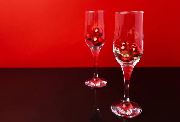 Twee champagne glazen met kleine kerstballen binnen tegen rode achtergrond — Stockfoto
