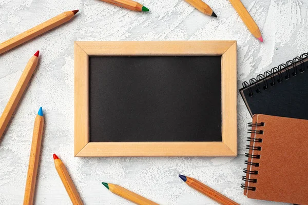 Klein schoolbord in houten frame omgeven door kleurpotloden — Stockfoto