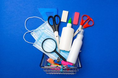 Okul malzemeleri mavi arka planda bir alışveriş arabasında.