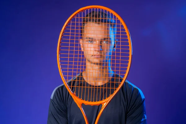 Caucasian young man tennis player posing with tennis racket against purple background