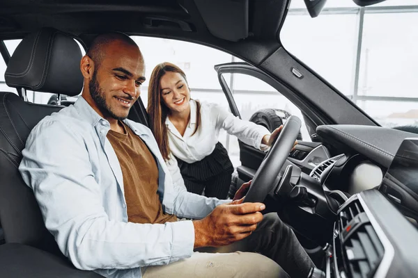 Joven vendedora atractiva en sala de exposición de coches mostrando un coche a su cliente masculino — Foto de Stock