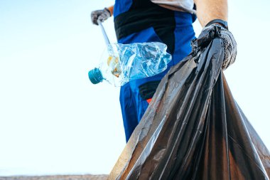 Plajı temizleyen bir çöp torbasına plastik çöp atan gönüllü bir adam.