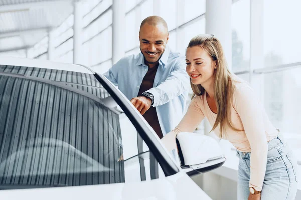 Jovem casal feliz escolhendo um carro na concessionária de carros — Fotografia de Stock