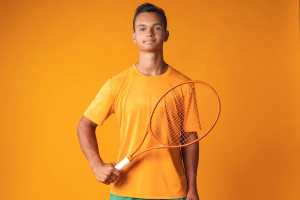 オレンジを背景にラケットを持っている若いテニス選手のスタジオショット — ストック写真