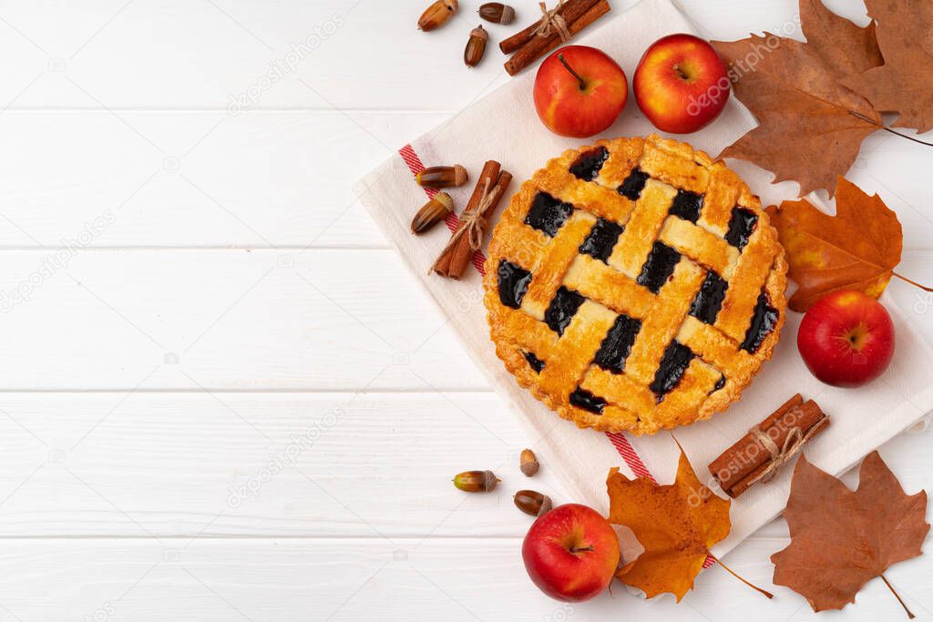 Autumn thankgiving pie on white wooden board decorated with dry leaves and cinnamon sticks