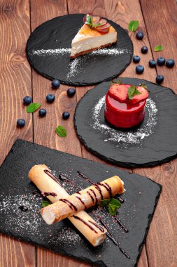 Tahta masadaki siyah tabakta servis edilen üç tatlı.