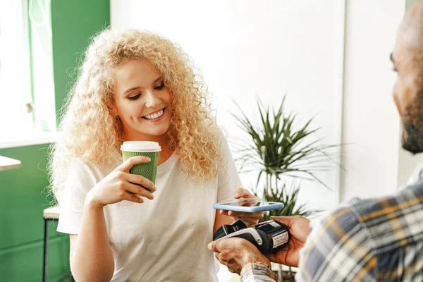 Kvinnlig kund till kafé betalar för kaffe via mobiltelefon med kontaktlös teknik — Stockfoto