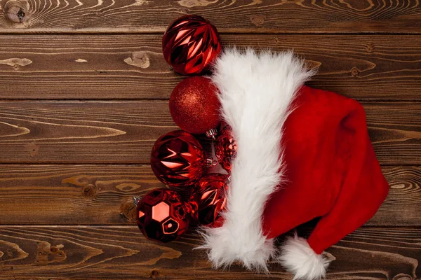 Kerstmuts en rode kerstballen op bruine houten achtergrond — Stockfoto