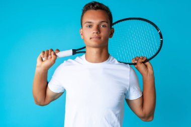 Spor giyim sektöründe genç bir tenisçi mavi arka planda poz veriyor.