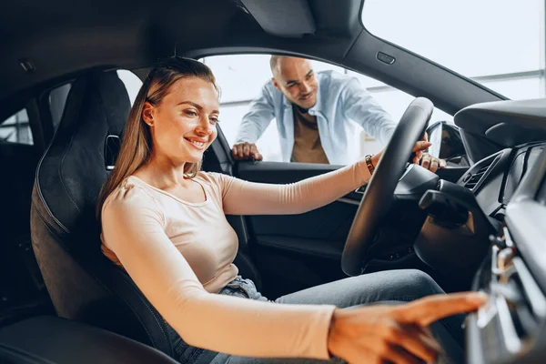 Joyful jovem casal olhando ao redor dentro de um carro novo que eles vão comprar em uma loja de carros — Fotografia de Stock