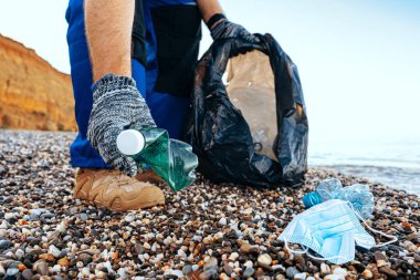 Plajı temizleyen bir çöp torbasına plastik çöp atan gönüllü bir adam.