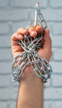 Metal zincire vurulmuş, elinde sigara tutan bir erkek.