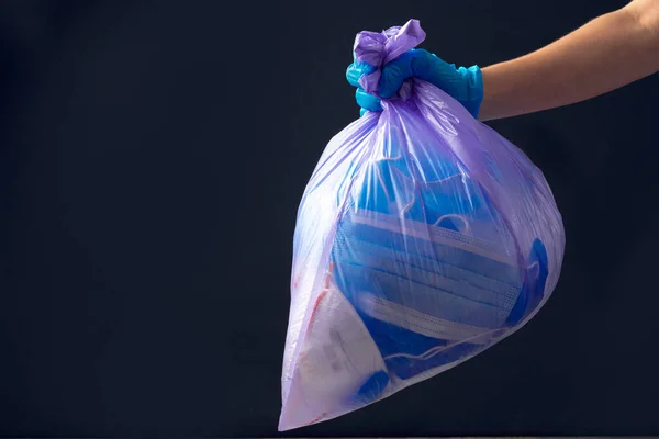 Χέρι στο ιατρικό γάντι ρίχνουν σακούλες σκουπιδιών. Η χρησιμοποιημένη μάσκα προσώπου. — Φωτογραφία Αρχείου