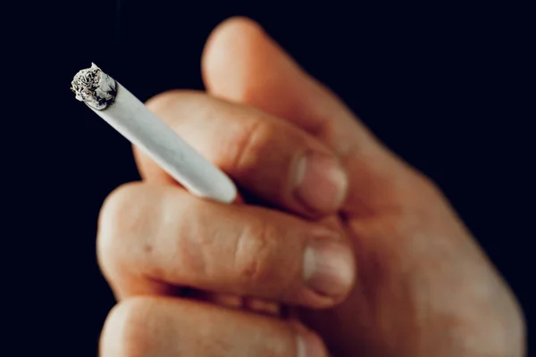 Mano masculina con un cigarrillo ardiente sobre fondo negro —  Fotos de Stock