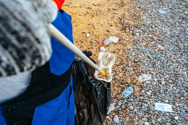 Photo rapprochée d'un homme ramassant des ordures avec un outil de saisie sur la plage — Photo