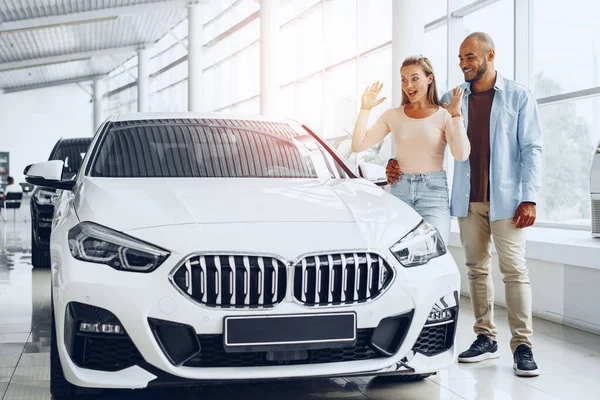 Jovem casal feliz escolhendo um carro na concessionária de carros — Fotografia de Stock