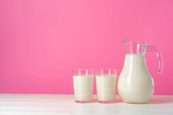 Vetreria con latte fresco su sfondo rosa pastello — Foto Stock