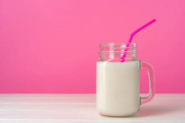 Γυάλινα σκεύη με φρέσκο γάλα σε ροζ παστέλ φόντο — Φωτογραφία Αρχείου