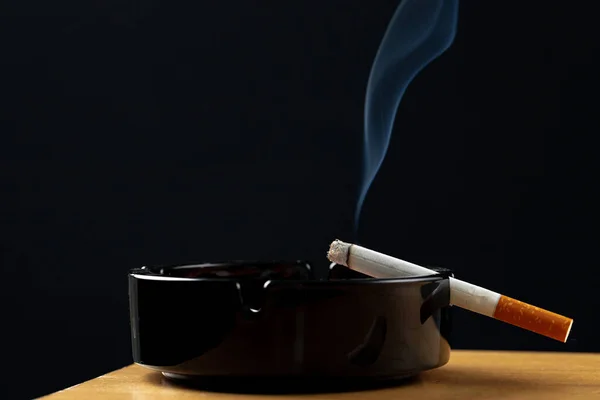 Burning cigarette in a black ash tray