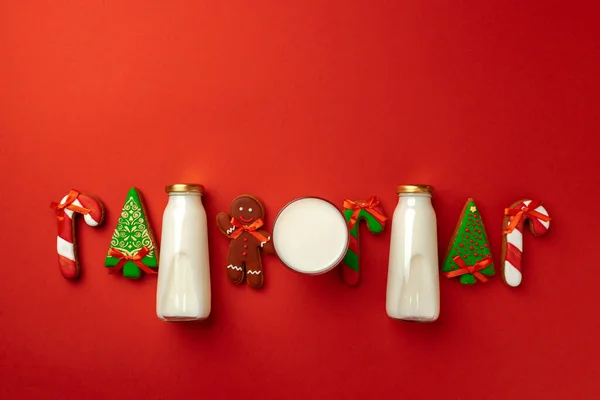 Glasmilchflasche und weihnachtliche Lebkuchen auf rotem Hintergrund — Stockfoto