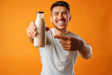 Happy smiling mixed-race man holding milk against yellow background clipart