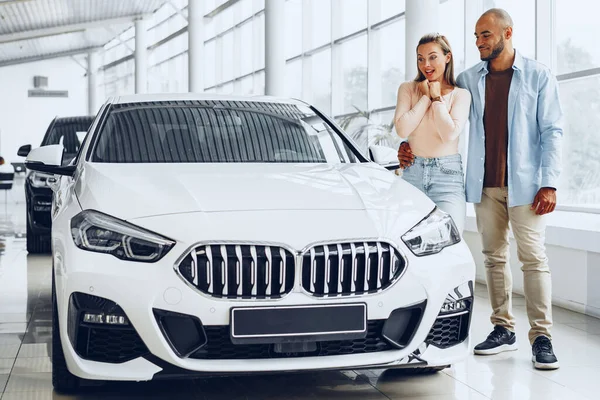 Jovem casal feliz escolhendo um carro na concessionária de carros — Fotografia de Stock